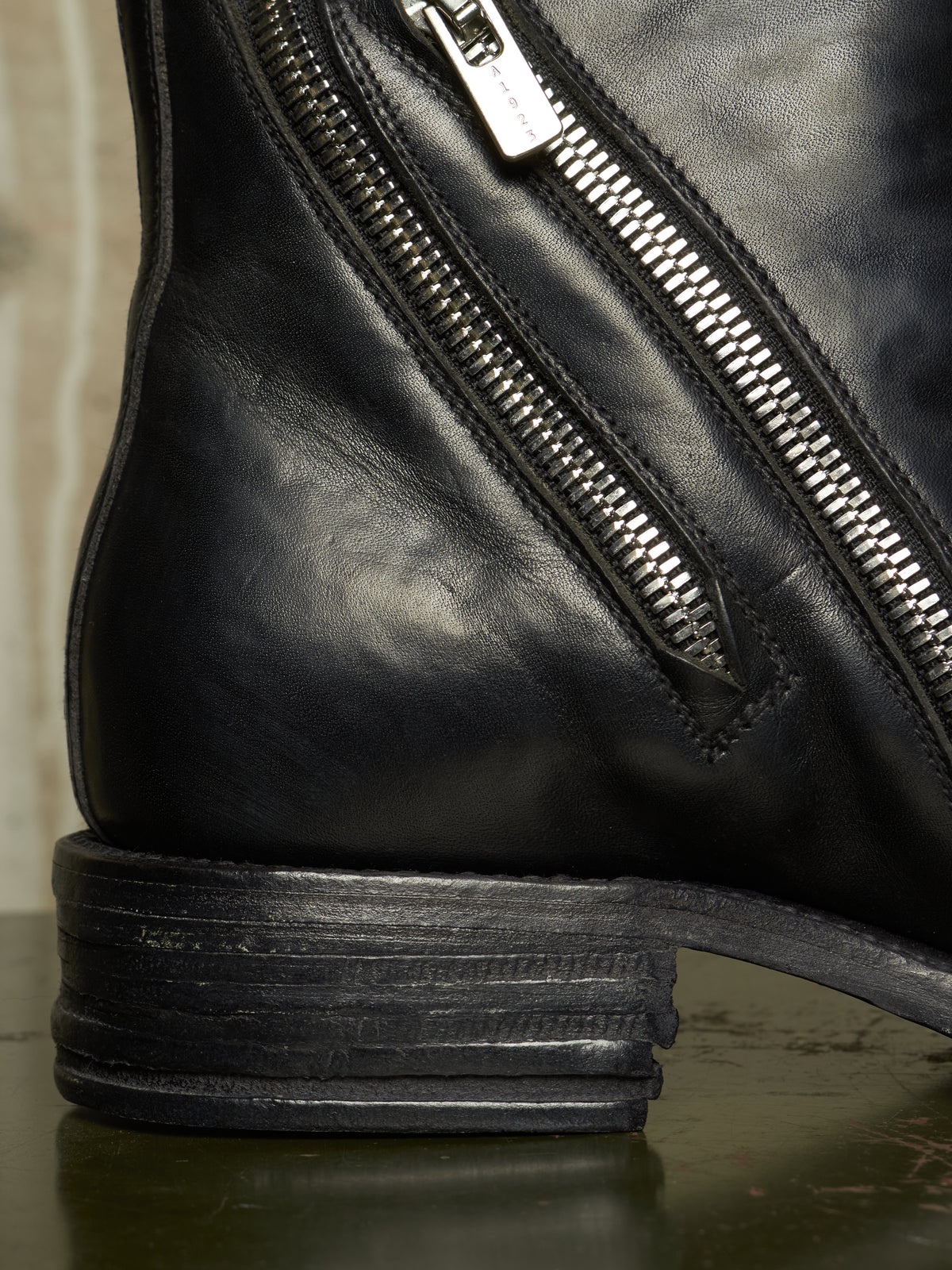 Close-up of a black leather boot showing the side zipper, stacked heel, and textured leather surface.