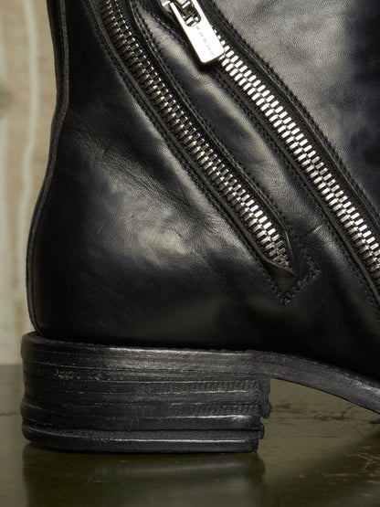 Close-up of a black leather boot showing the side zipper, stacked heel, and textured leather surface.