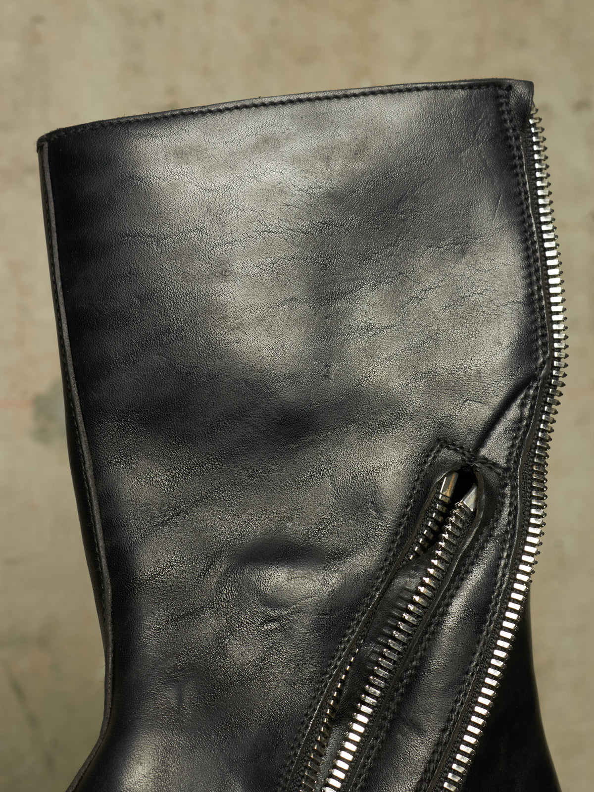 Close-up of a black leather boot featuring a prominent silver zipper running vertically along the side.