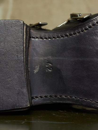 Close-up of the heel and side of a dark leather boot, showing stitched edges, a metal buckle, and an embossed size marking on the insole.