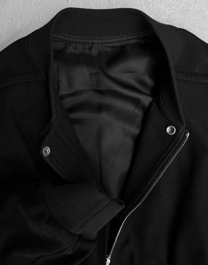A close-up of the Rick Owens SS24 “LIDO” Nubuck Leather Cropped Flight Bomber Jacket features a zipper, snap buttons, ribbed collar, cuffs, and hems. Partially unzipped, it reveals a smooth black lining in true avant-garde Rick Owens style.