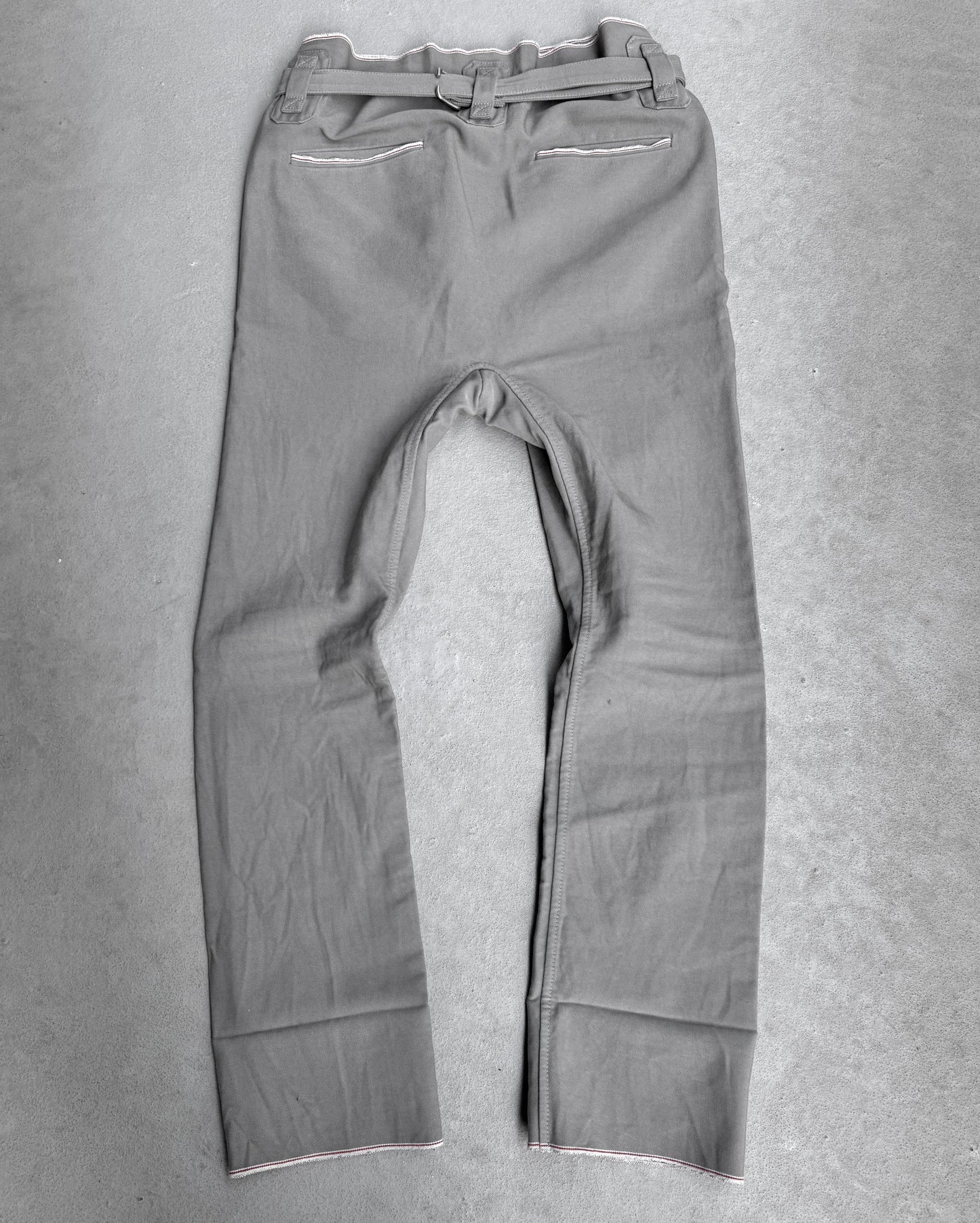 The Carol Christian Poell 2010 “IN-BETWEEN” PM/2578 PEDGE Self-edge High-waisted Metre Pants are shown laid flat on a light gray surface, back view, highlighting the brands avant-garde approach and distinctive material use.