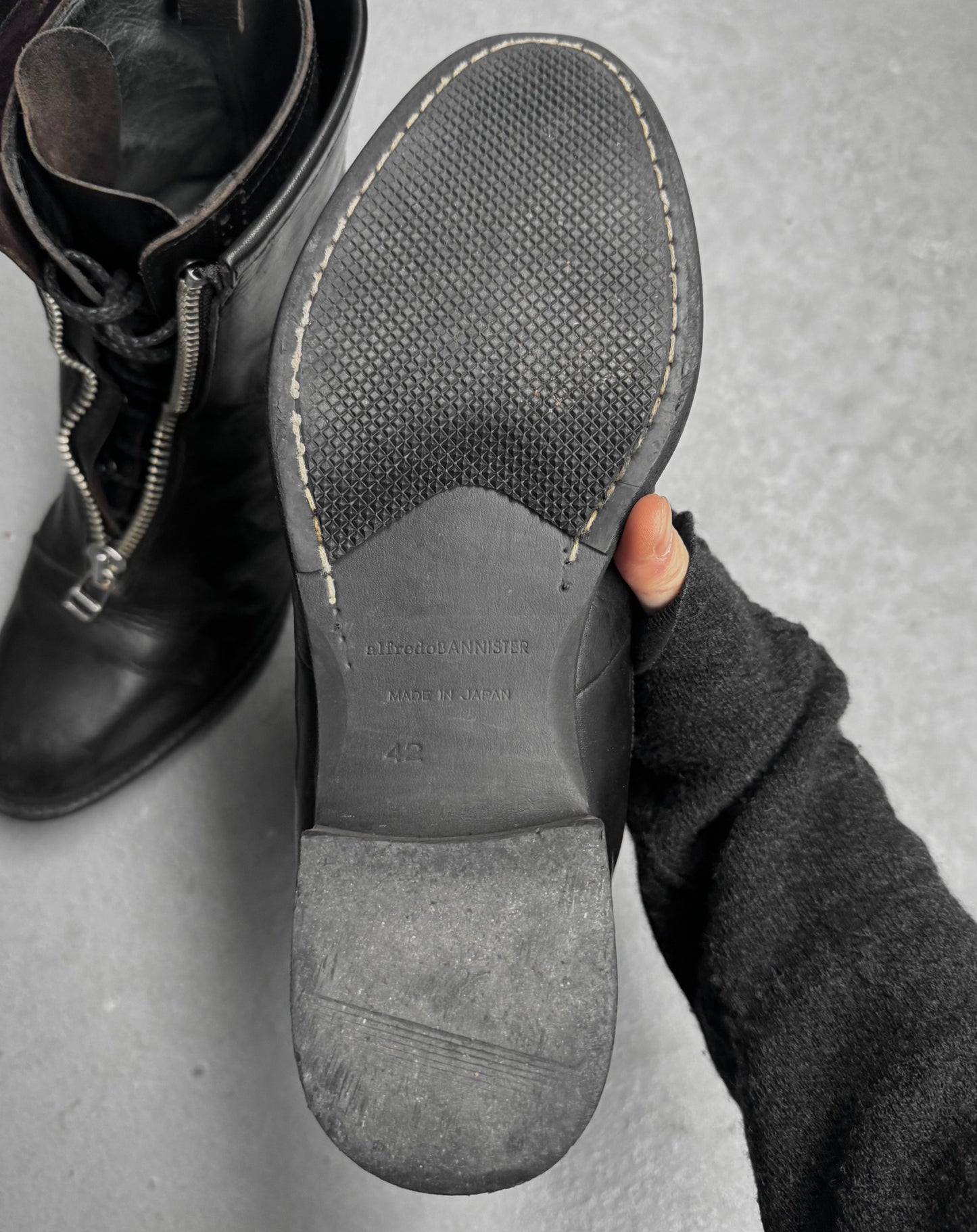 Close-up of a black leather boot sole with visible stitching on a gray background