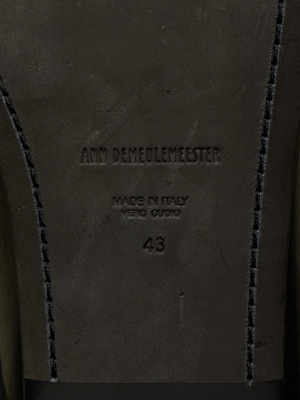 Close-up of the insole of a dark brown leather shoe, showing the embossed brand name 'Ann Demeulemeester', 'Made in Italy Vero Cuore', size '43', and decorative contrast stitching.