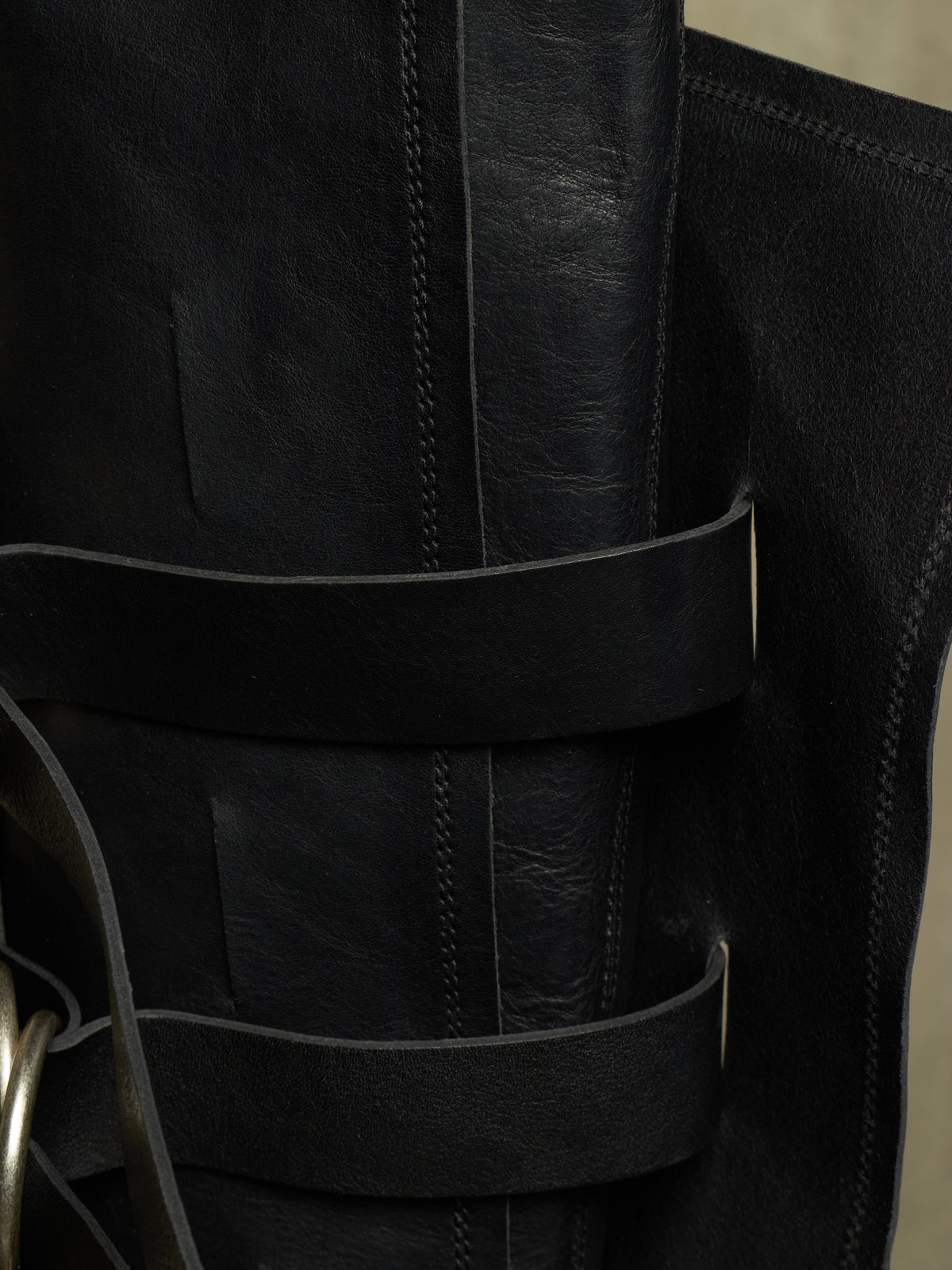 Close-up of a black leather boot with multiple horizontal straps and a metal ring detail on the side.