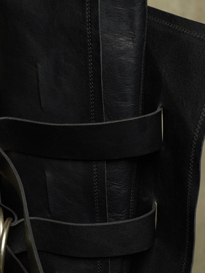Close-up of a black leather boot with multiple horizontal straps and a metal ring detail on the side.