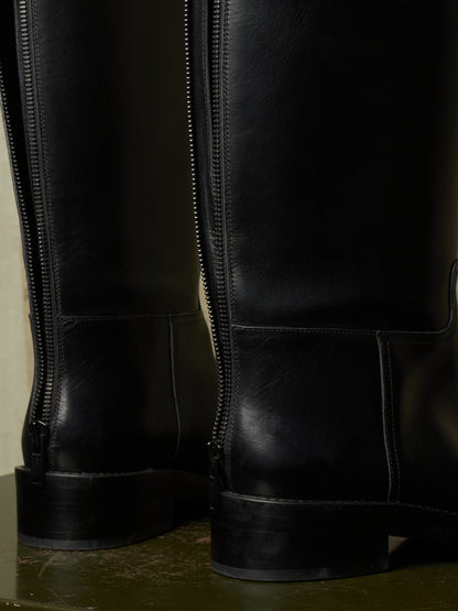 Close-up of the back zipper and heel area of a pair of black leather riding boots, showing the side profile and stitching details.