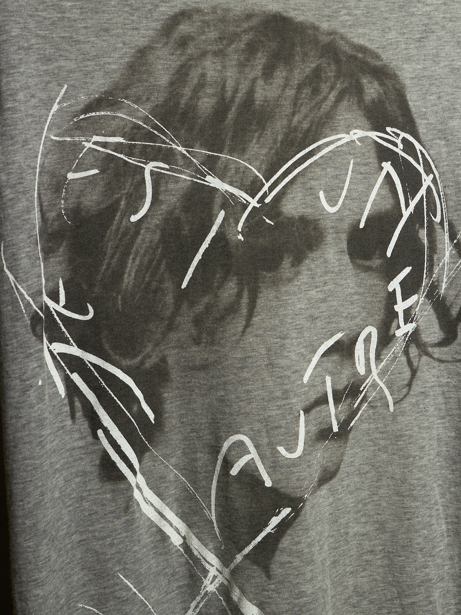 Close-up of a gray heather graphic print featuring a dark, sketchy portrait with white scribbled text and lines overlaid across the face.