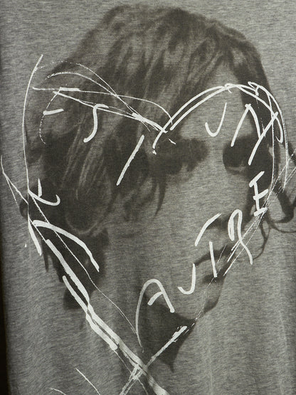 Close-up of a gray heather graphic print featuring a dark, sketchy portrait with white scribbled text and lines overlaid across the face.