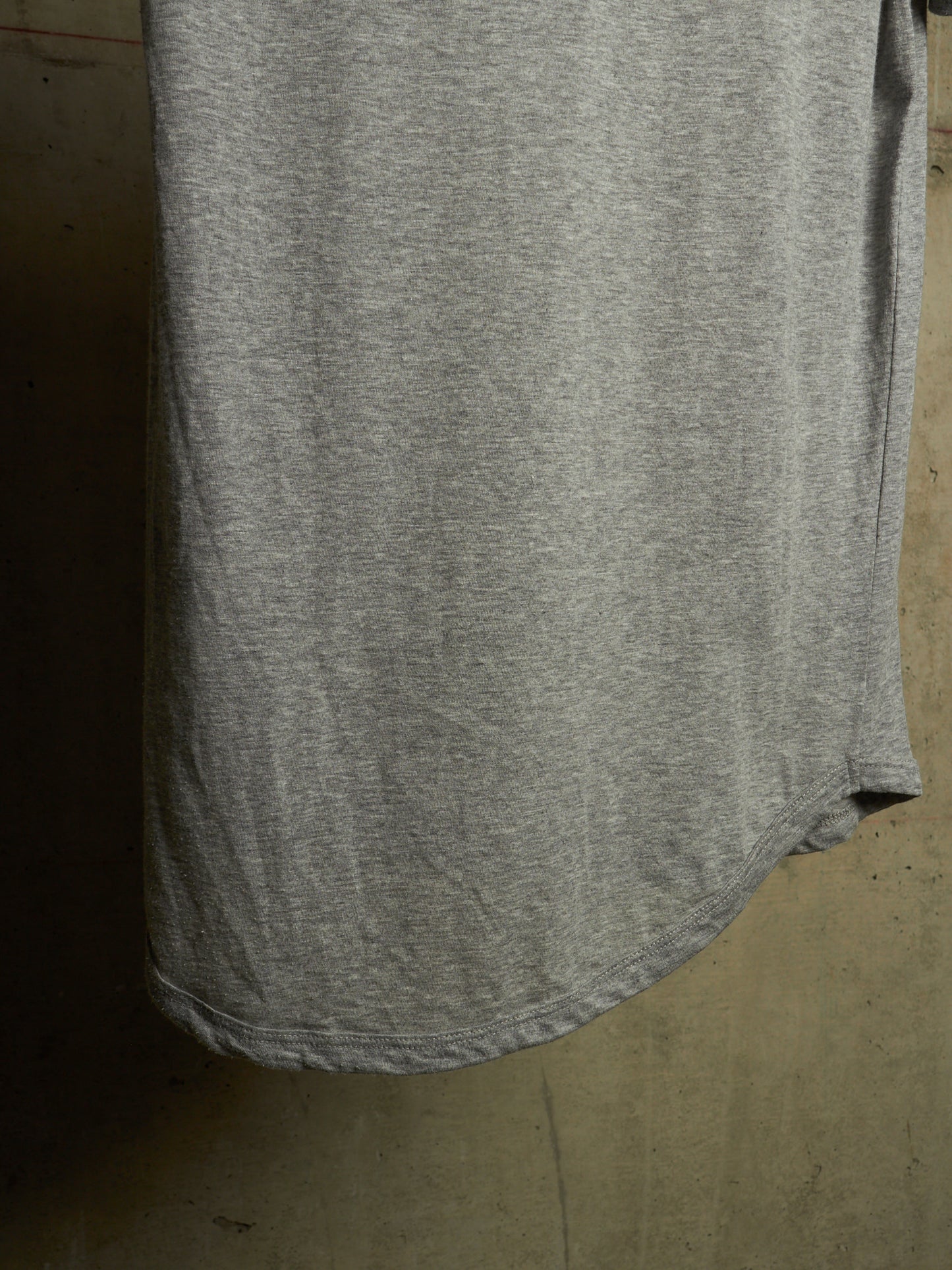 A close-up of a heather gray t-shirt hanging against a textured concrete wall.