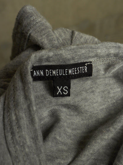 Close-up of a gray knit garment showing a black brand label that reads ANN DEMAULEMEESTER and a smaller size label reading XS.