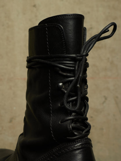 Close-up of a black leather lace-up boot against a textured beige background.