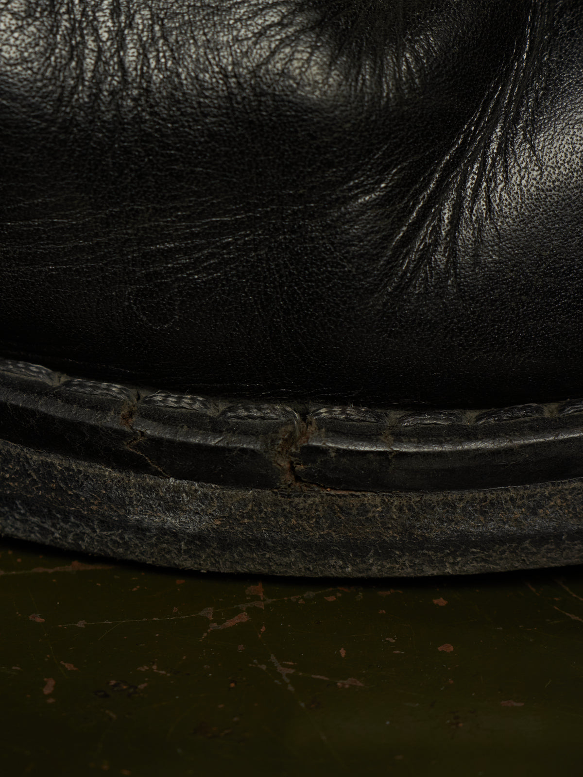 Close-up detail of a black leather boot or shoe sole with visible wear, scuffing, and texture against a dark green floor.