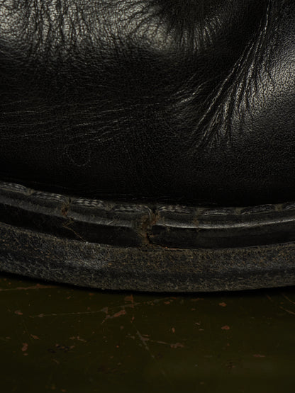 Close-up detail of a black leather boot or shoe sole with visible wear, scuffing, and texture against a dark green floor.