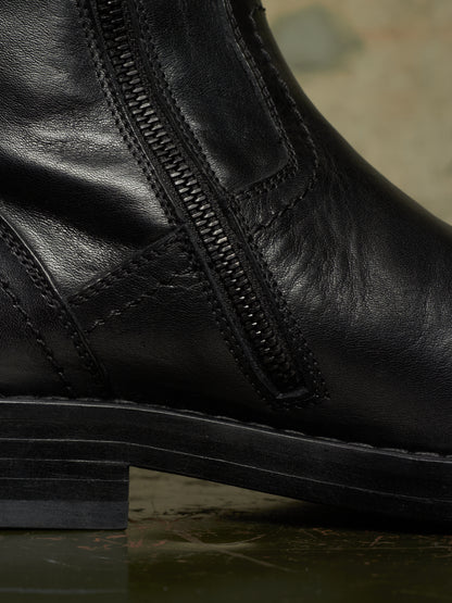 Close-up of a black leather ankle boot with a side zipper and stacked sole, photographed against a dark textured background.