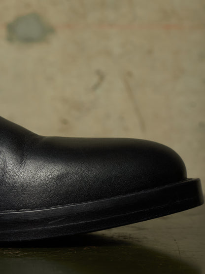 Close-up of the rounded toe and side of a black leather boot against a textured beige background.