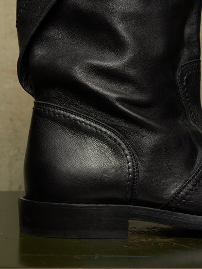 Close-up of a black leather boot showing the side heel, stitching, and textured leather surface.
