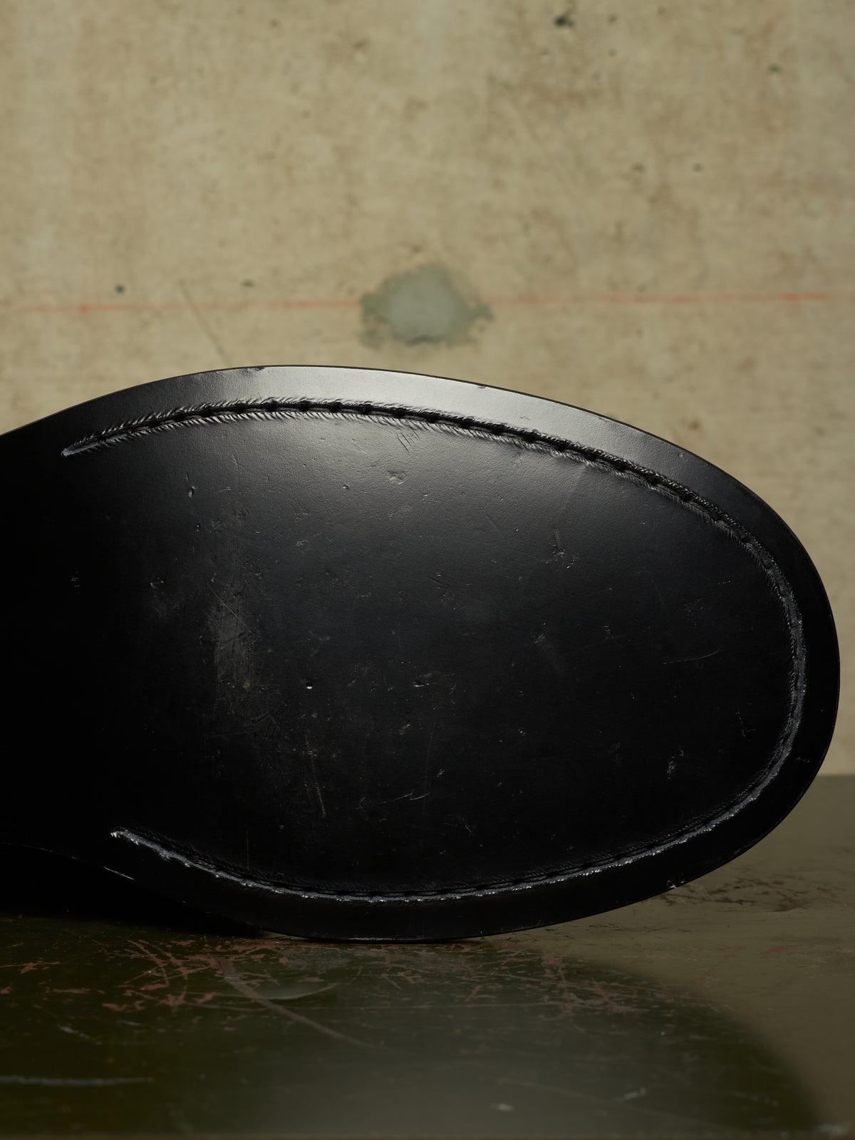 Close-up of the black leather sole of a shoe, showing the stitched edge, against a textured beige background.