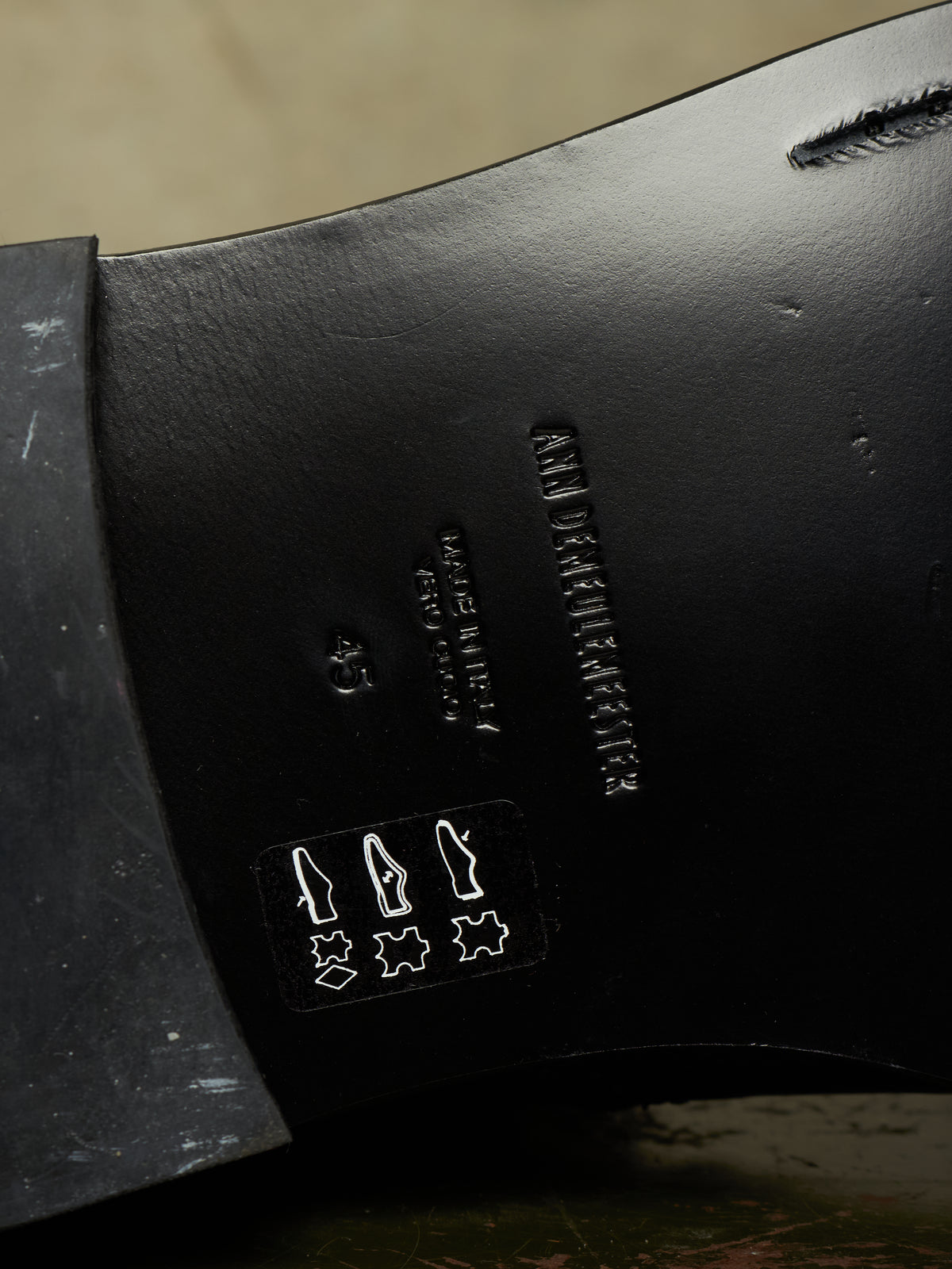Close-up of the black leather underside of a shoe, showing embossed branding and construction details.
