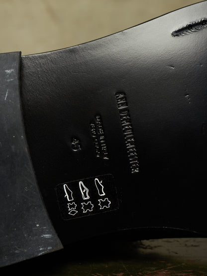 Close-up of the black leather underside of a shoe, showing embossed branding and construction details.