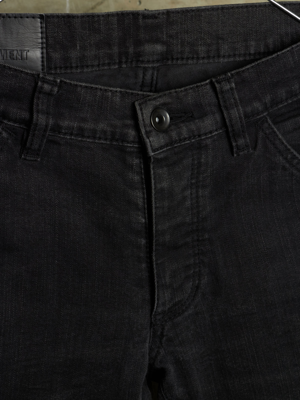 Close-up of black denim jeans showing the waistband, button closure, belt loops, and front pocket area.