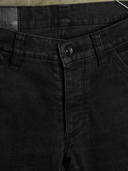 Close-up of black denim jeans showing the waistband, button closure, belt loops, and front pocket area.