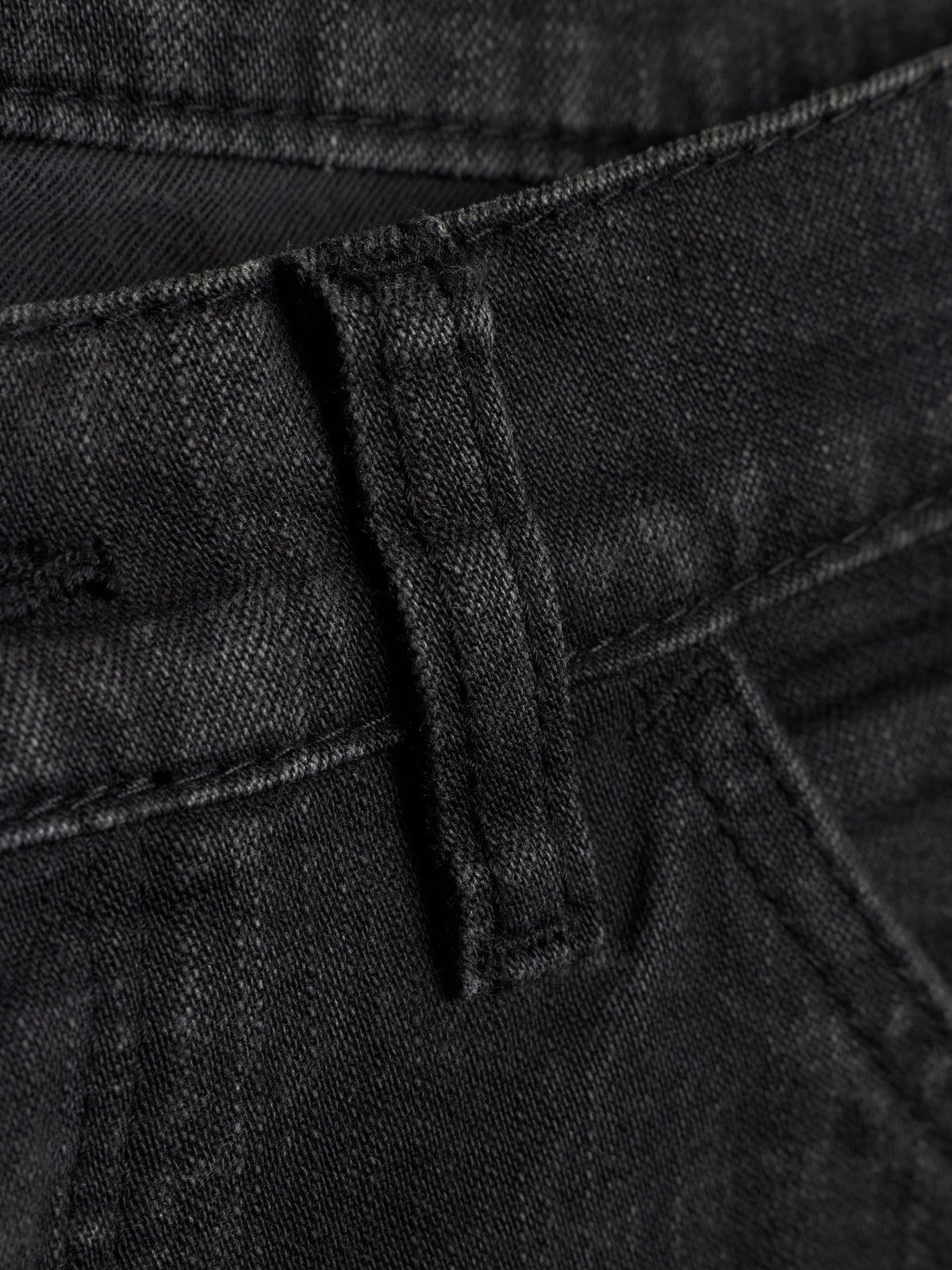 Close-up detail of black denim jeans showing the belt loop, waistband stitching, and fabric texture.