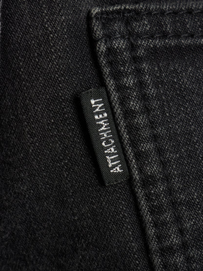 Close-up of black denim fabric with a small black brand tab reading ATTACHMENT stitched on the side.