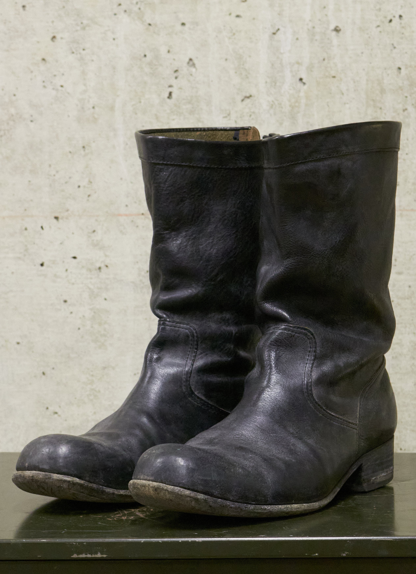 Pair of black leather boots on a textured surface with a neutral background