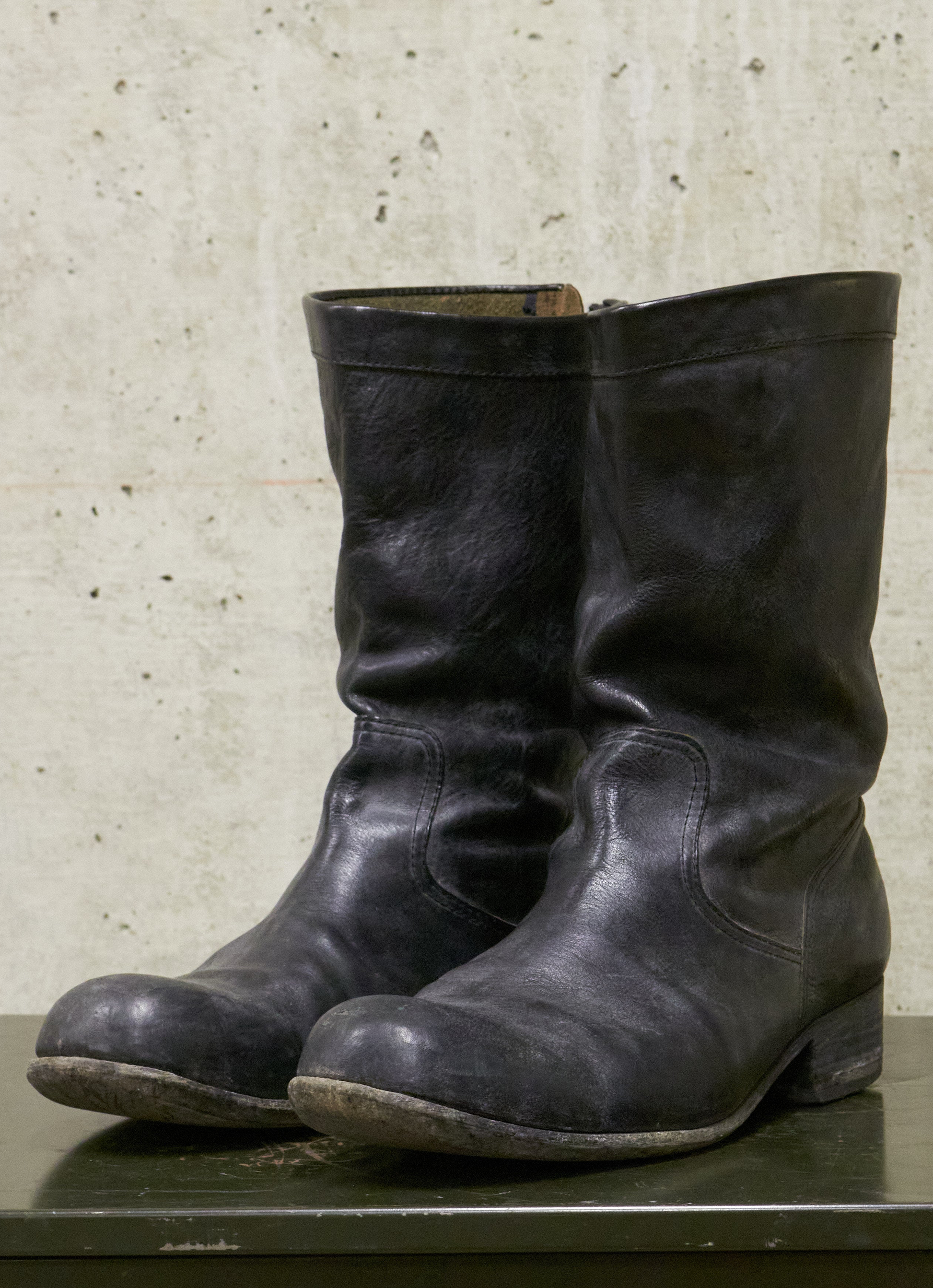 Pair of black leather boots on a textured surface with a neutral background