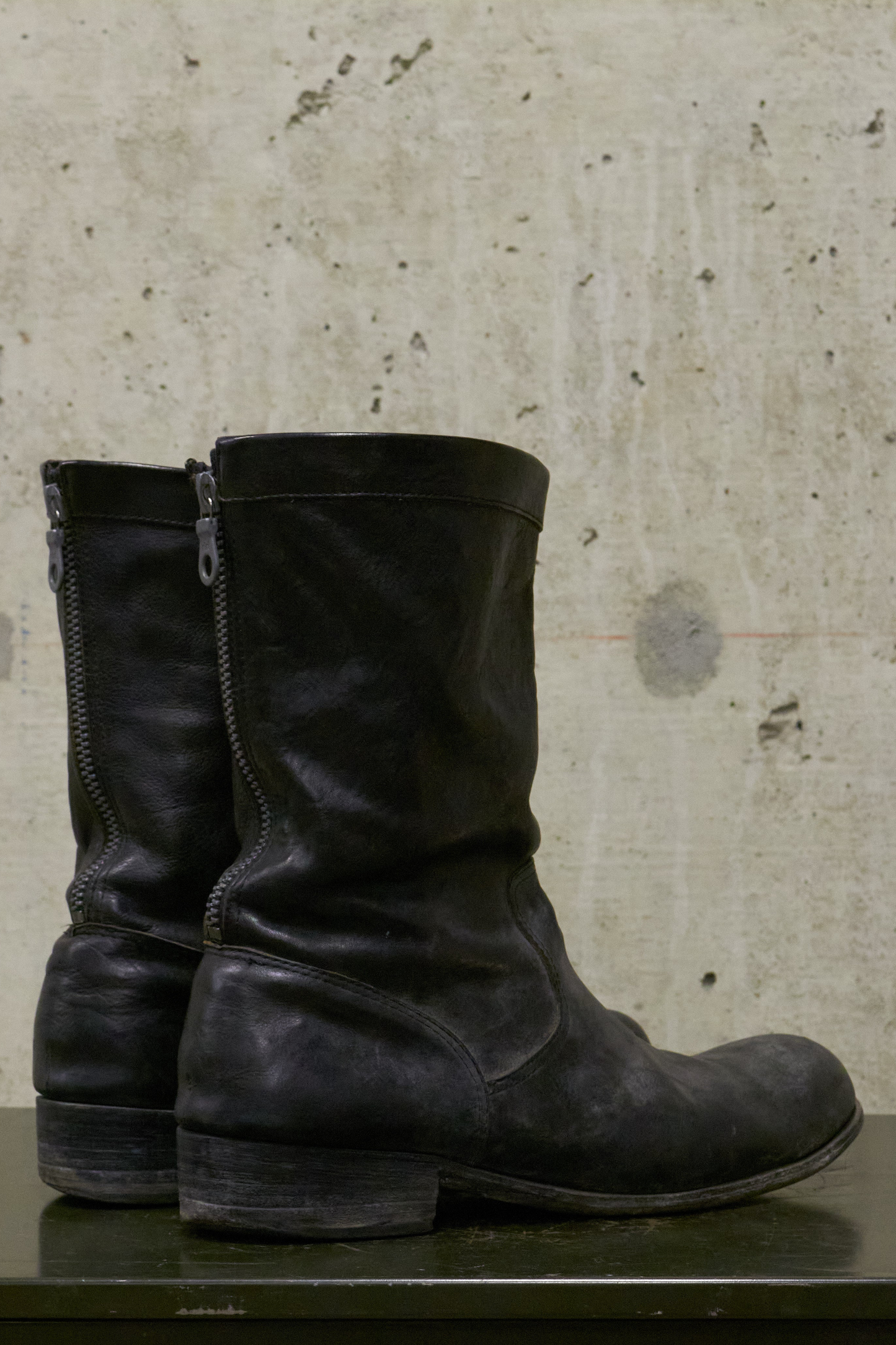 Pair of black leather boots on a textured surface with a concrete wall background