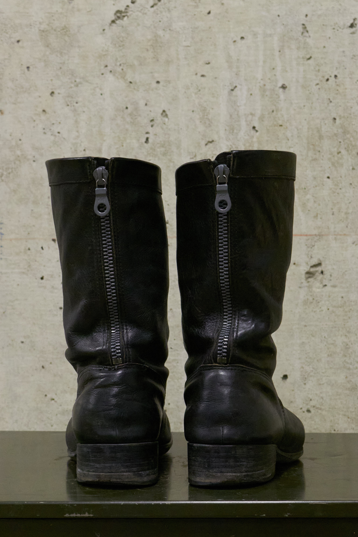 Pair of black leather boots with zippers on a textured surface.