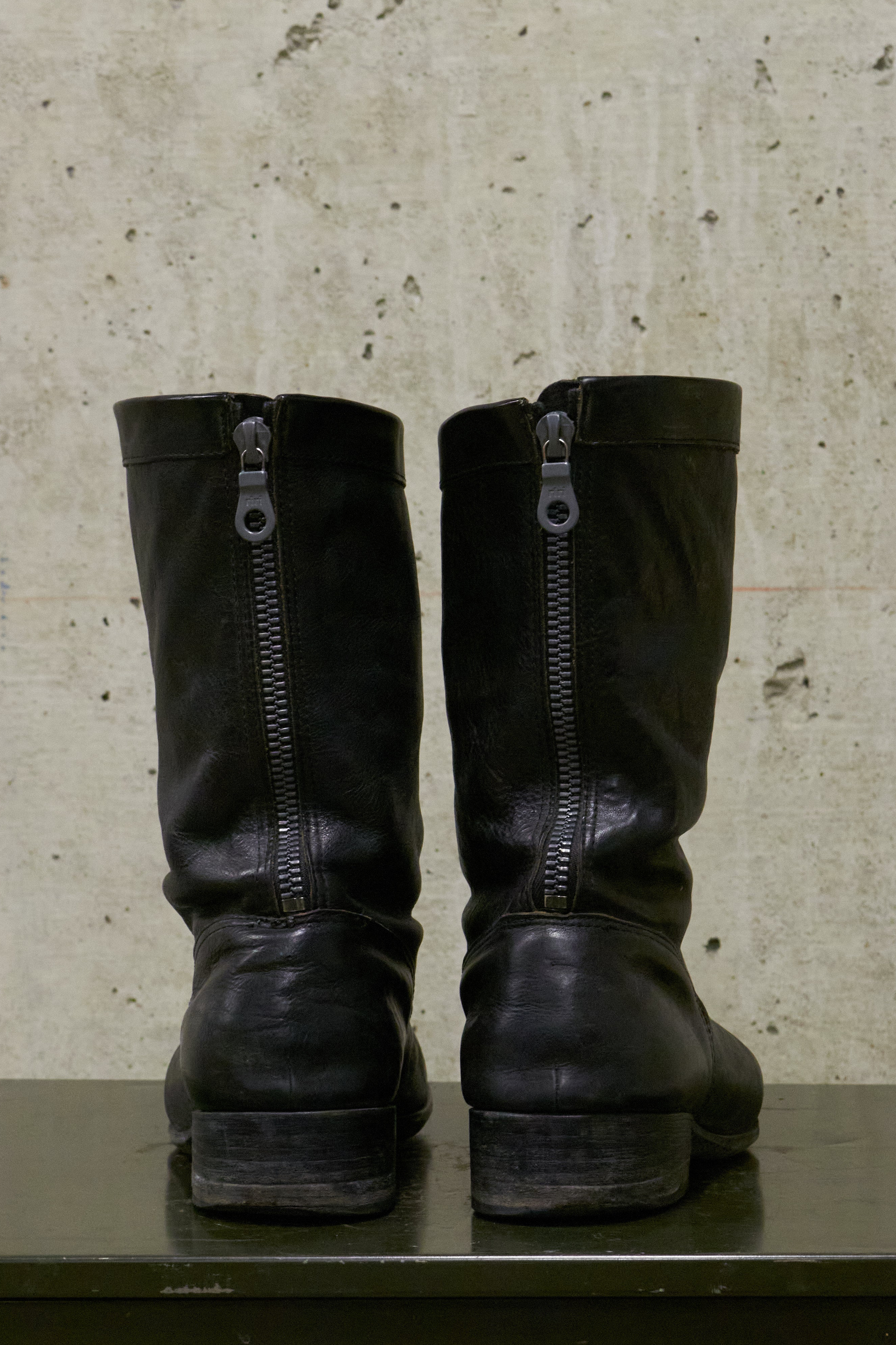 Pair of black leather boots with zippers on a textured surface.