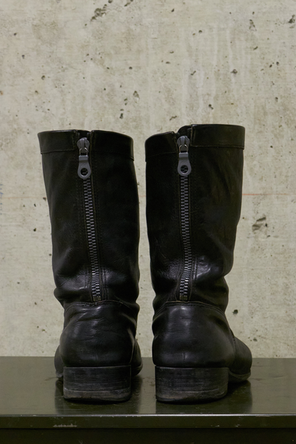 Pair of black leather boots with zippers on a textured surface.