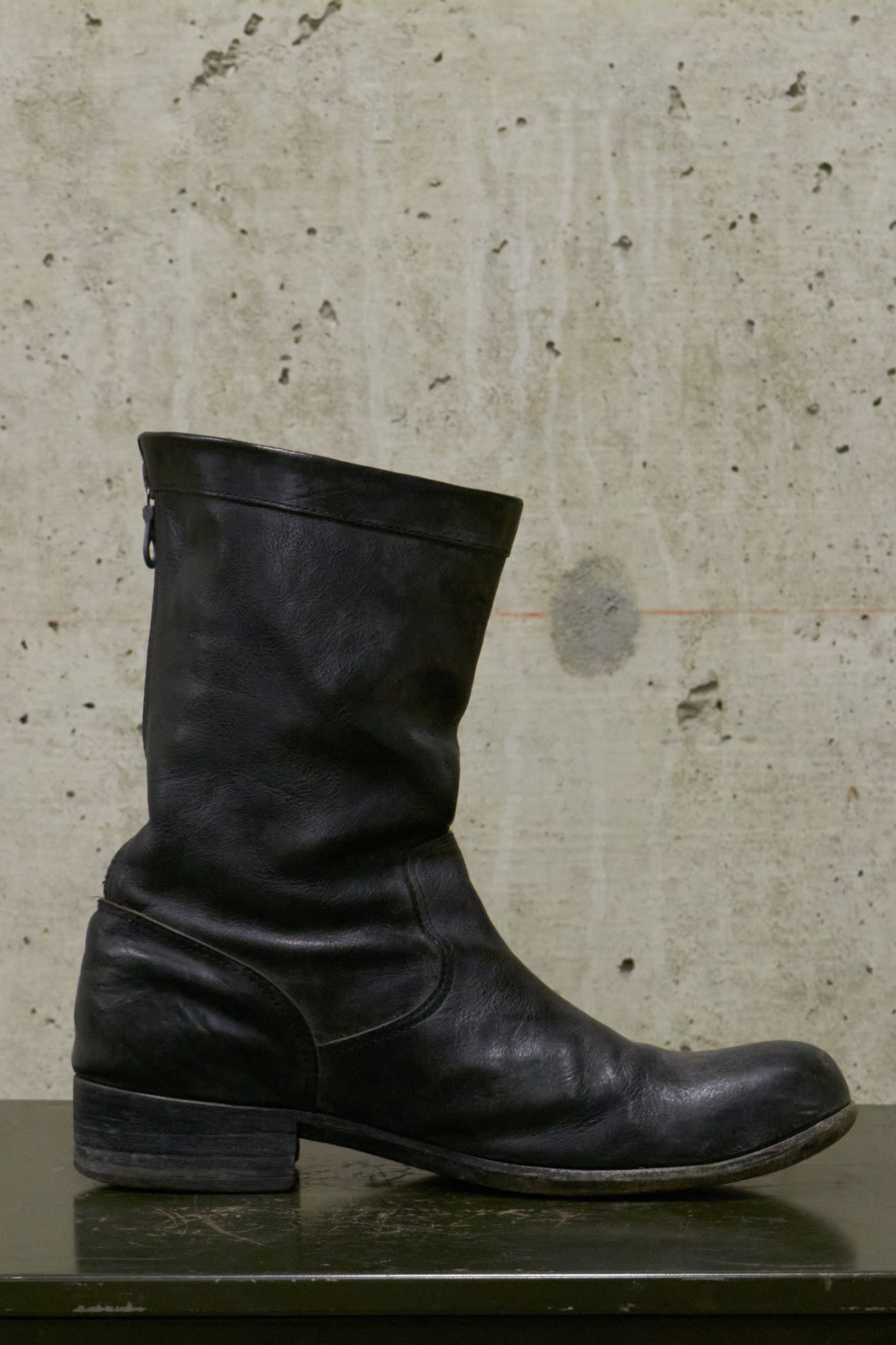 Black leather boot on a textured surface with a neutral background