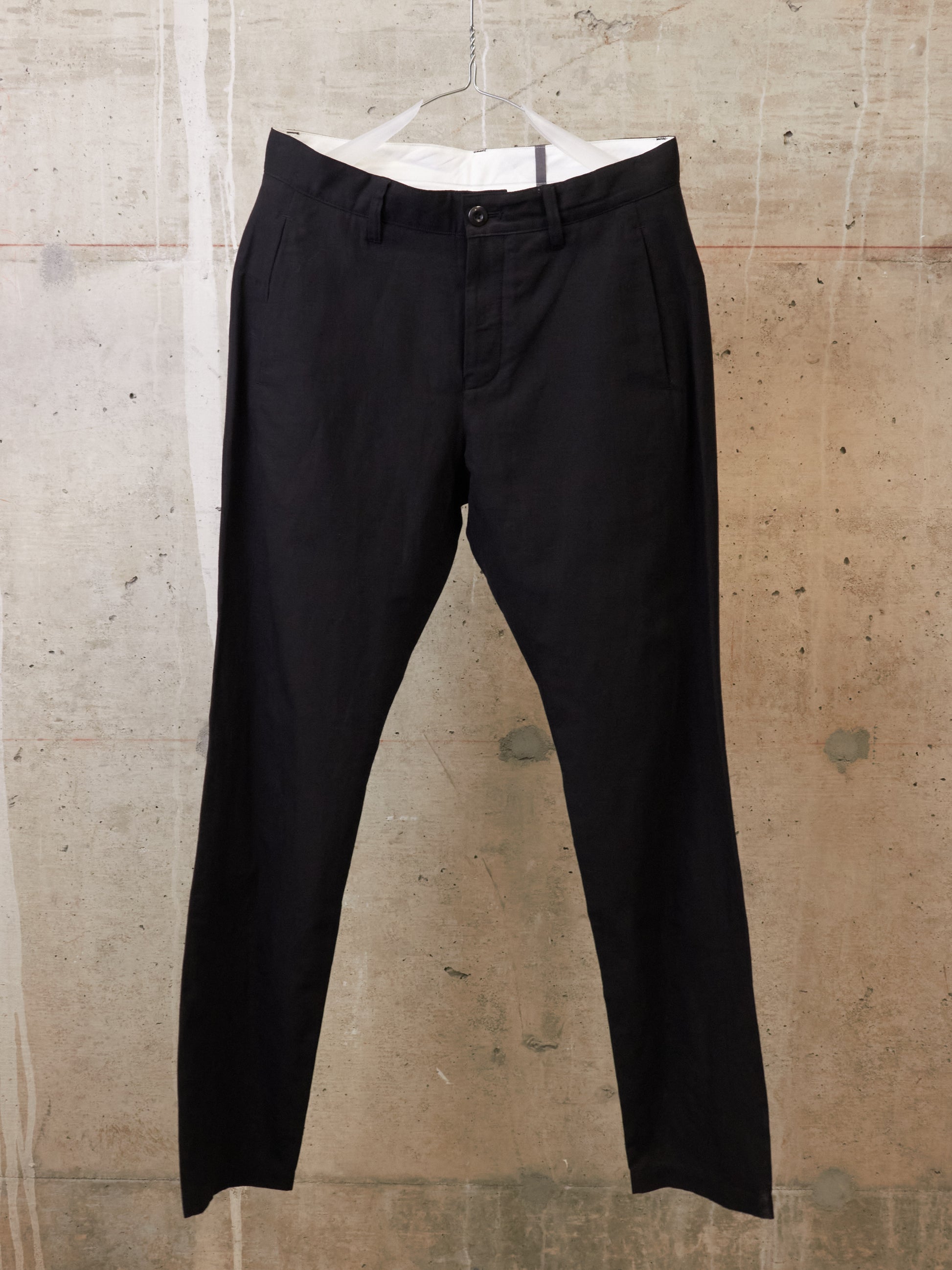 Black pants on a hanger against a textured beige wall
