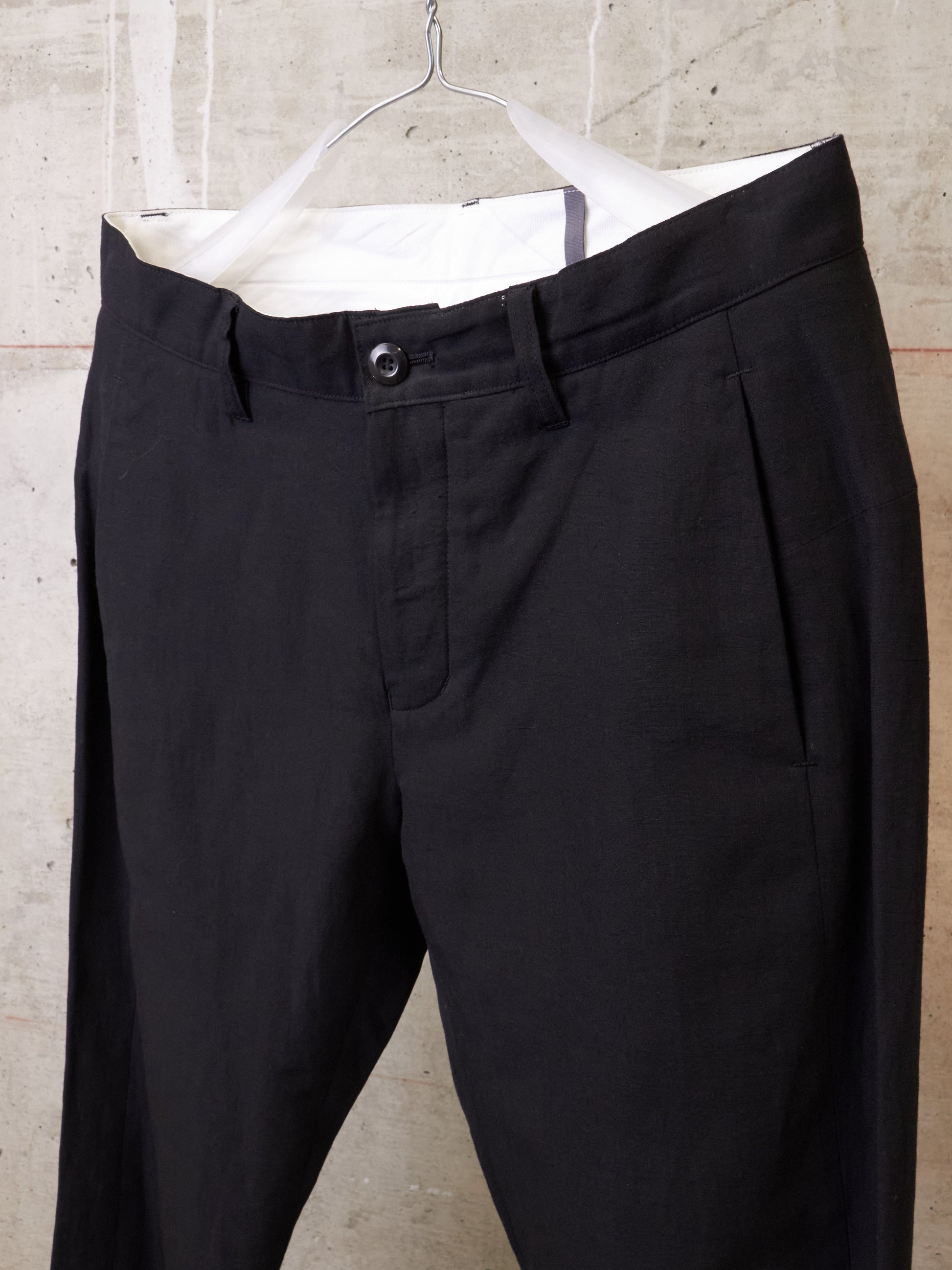 Black pants hanging on a hanger against a concrete wall.