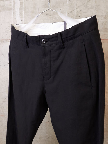 Black pants hanging on a hanger against a concrete wall.