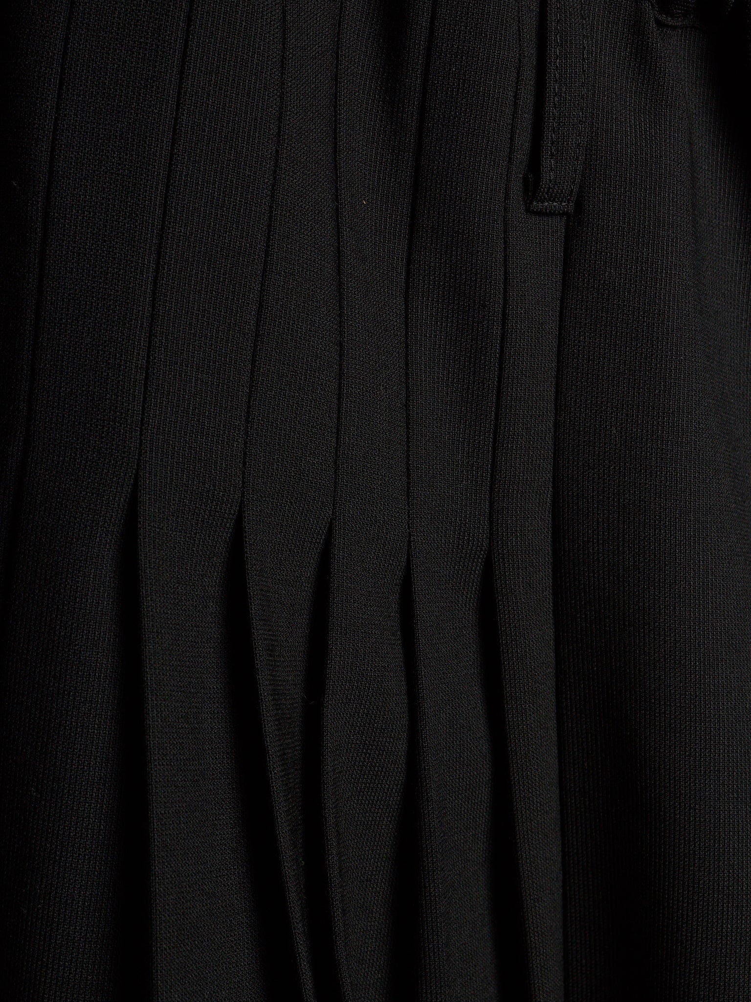 Close-up of a black pleated fabric garment, showing vertical pleats and a small tab detail.
