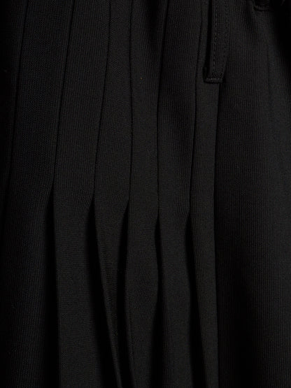 Close-up of a black pleated fabric garment, showing vertical pleats and a small tab detail.
