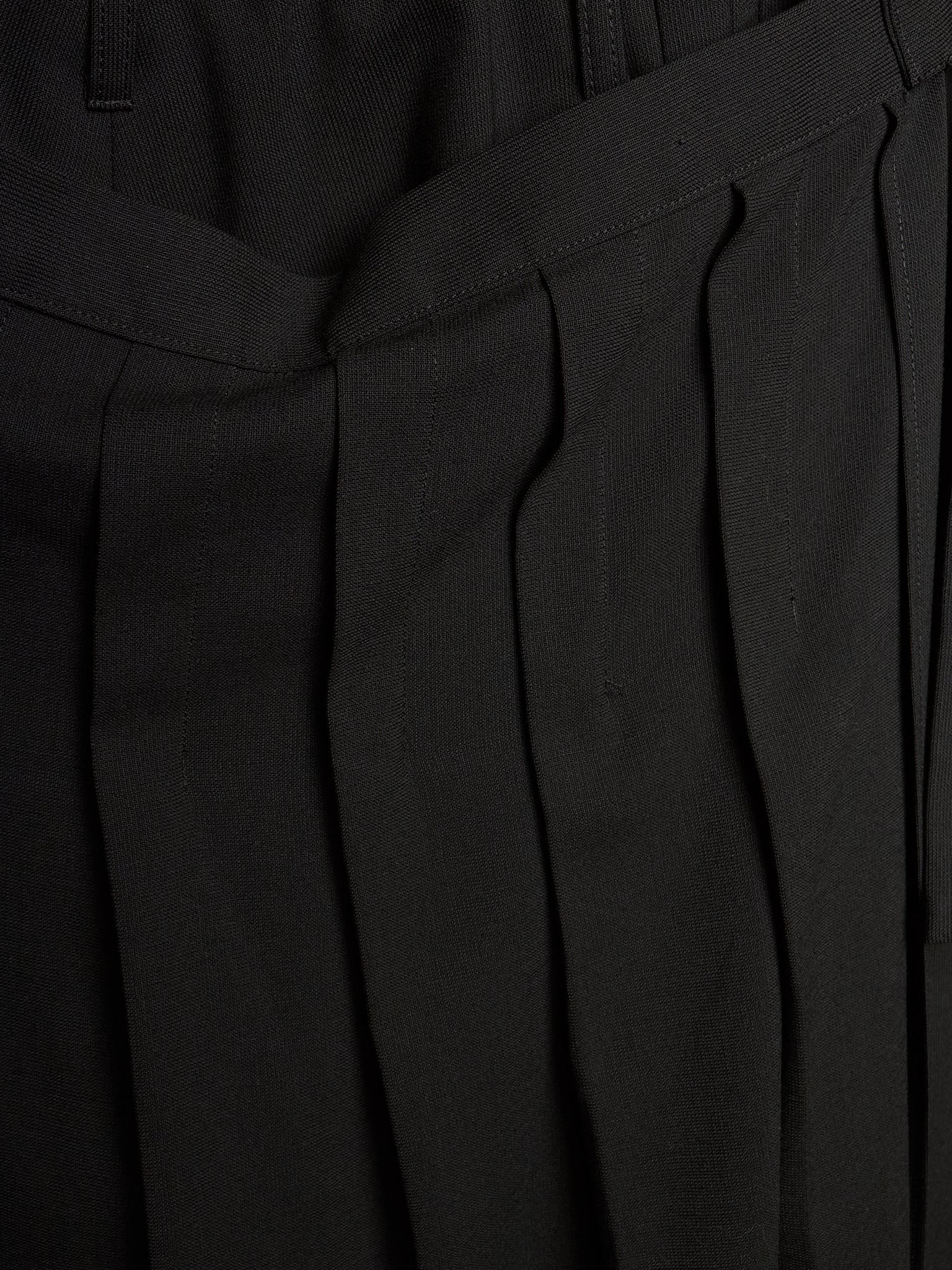 Close-up of black pleated trousers showing the fabric texture and waistband details.