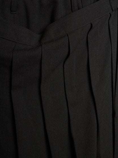 Close-up of black pleated trousers showing the fabric texture and waistband details.