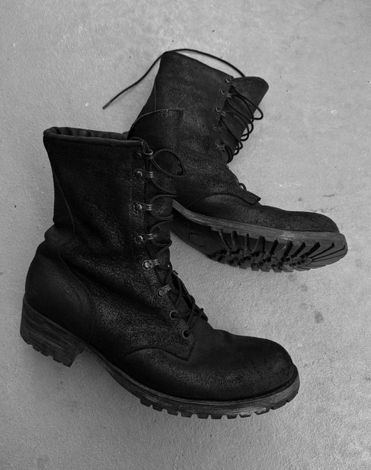 ATTACHMENT by Kazuyuki Kumagai Reversed Cow Leather Lace-up Boots feature thick soles and rugged style, adding a bold edge to any menswear look. Shown here in black, placed on a light, textured surface.