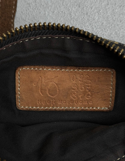 A close-up of an embossed leather label sewn inside a yellow Kyoji Maruyama Early 00s crocodile-embossed side bag, showing “Kyoji Maruyama” and some numbers above the name. A brass zipper is visible at the top.