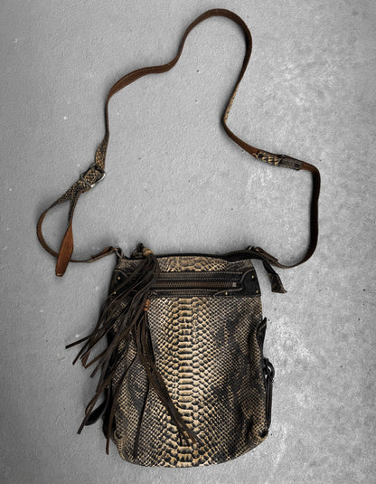A Kyoji Maruyama Early 00s Yellow Crocodile Embossed Leather Side Bag with a long, adjustable strap and front zipper pocket rests on a gray textured surface. This Japanese designer bag features decorative leather fringes.
