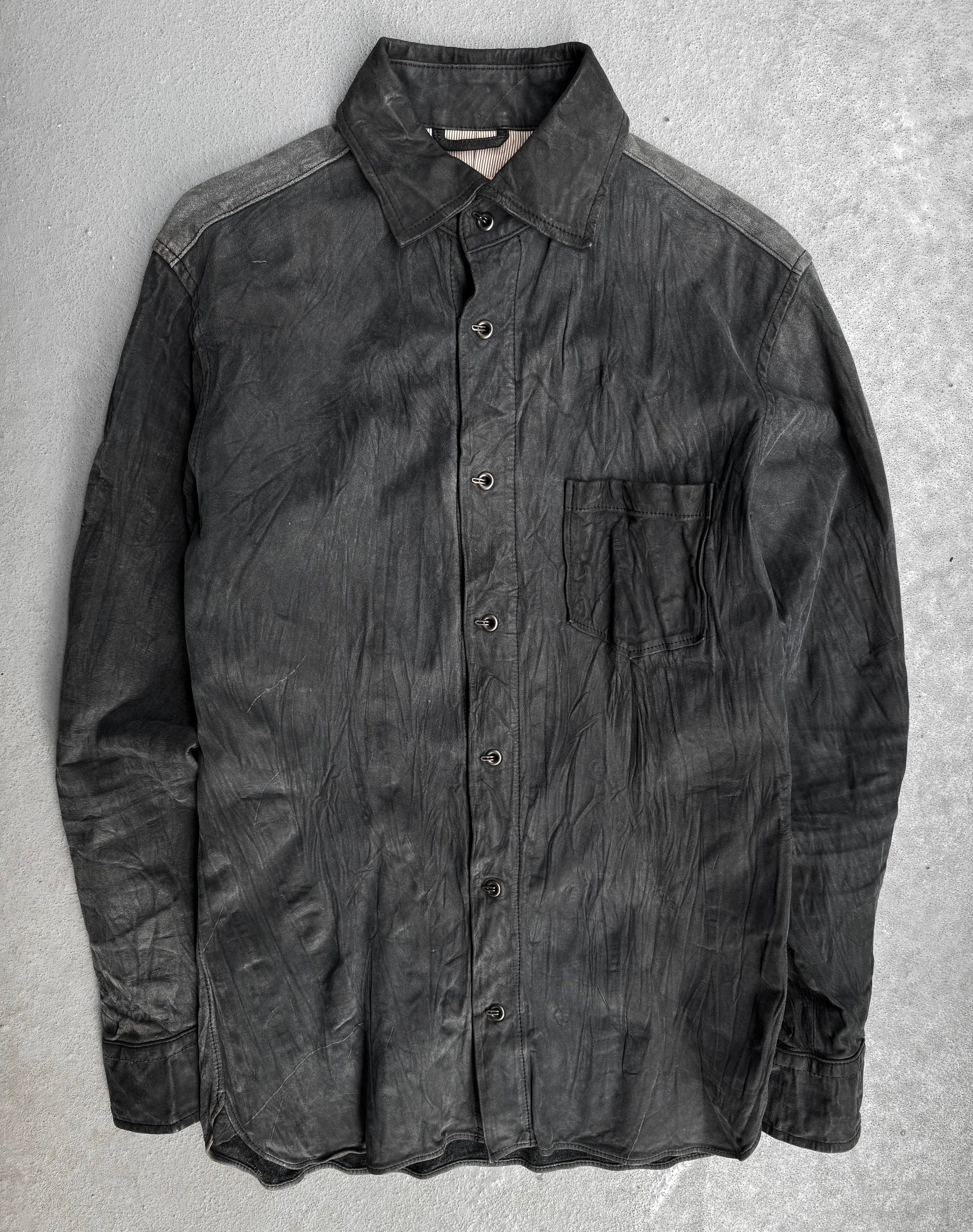 The Kyoji Maruyama Early 00s Washable Wrinkle Nubuck Leather Shirt is a black, long-sleeve button-up with a single chest pocket, shown slightly wrinkled and laid flat on a light gray textured surface.
