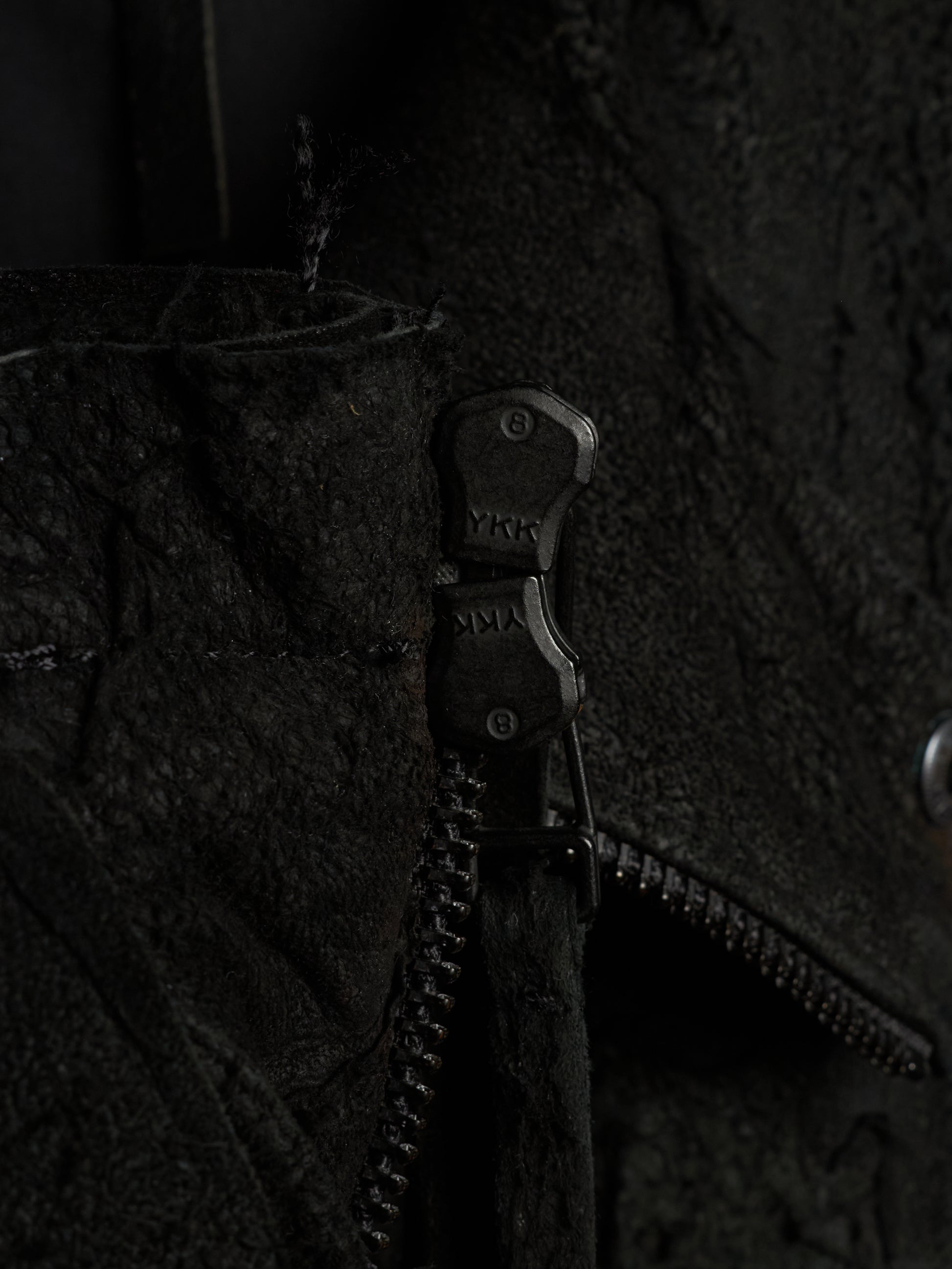 Close-up of a black textured jacket with a black metal zipper featuring the brand name 'YKK' on the pull tab.