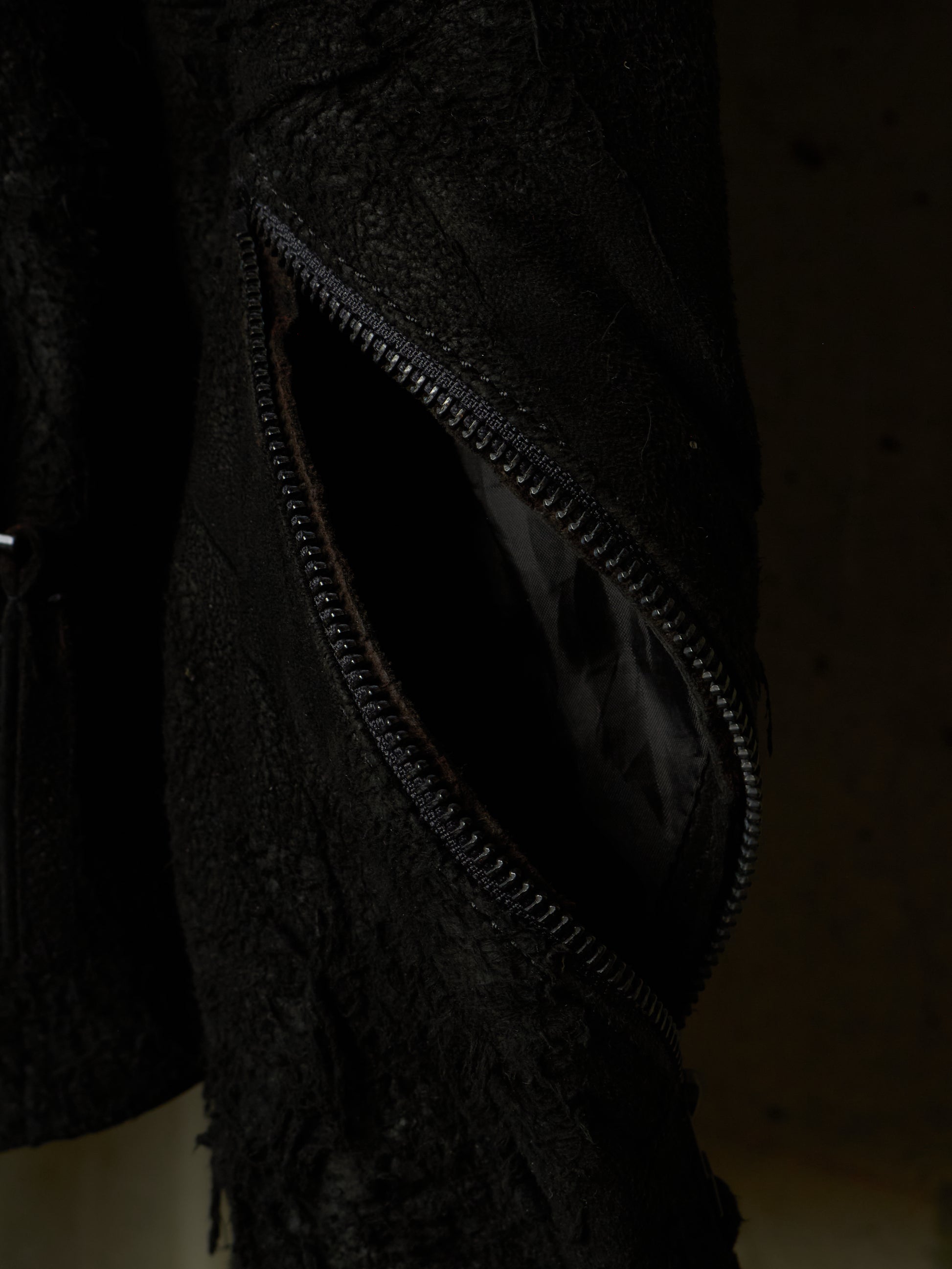 Close-up of a black textured jacket or coat with a partially unzipped pocket, showing a dark interior lining.
