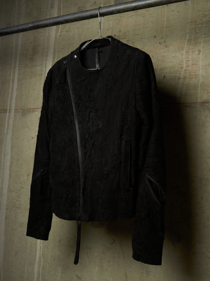 A black textured jacket with a diagonal zipper, hanging on a metal hanger from a horizontal rod against a concrete wall.