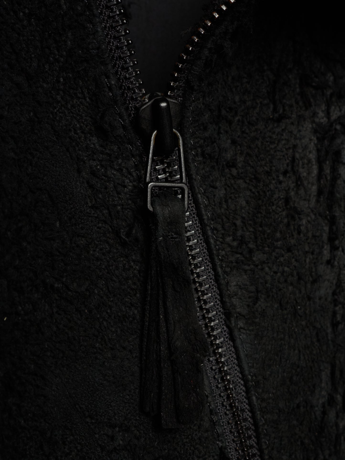 Close-up of a black textured zippered jacket with a black tassel zipper pull and a silver-toned metal slider.